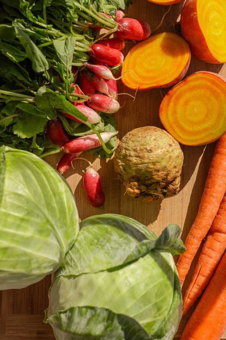 Raw vegetables laid out on a wooden cutting board before being chopped.