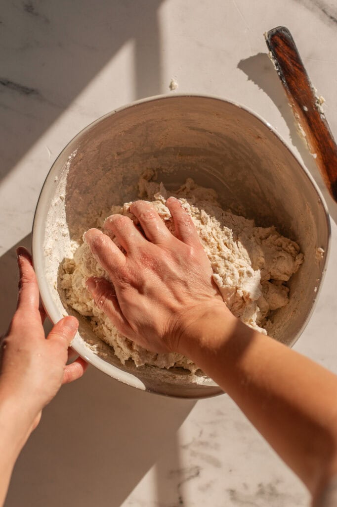 Hands mixing the ingredients of yogurt bagels into a shaggy dough ball.