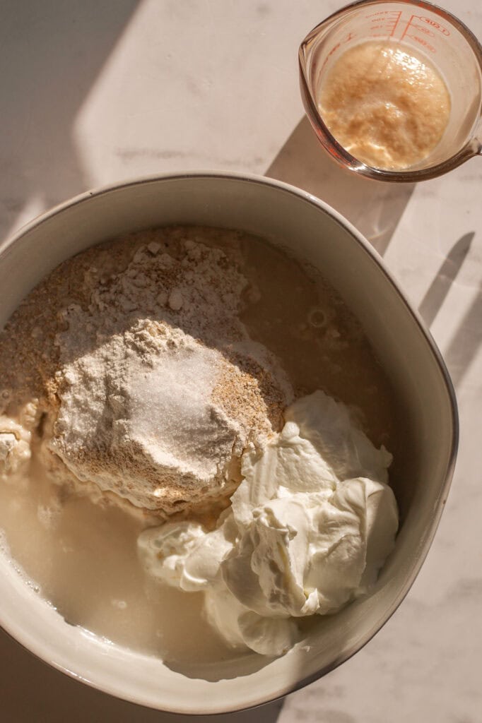 A bowl of raw ingredients including greek yogurt, bread flower, salt, water and instant yeast.
