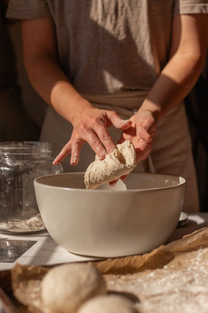 Close-up of hands stretching and folding small dough balls.