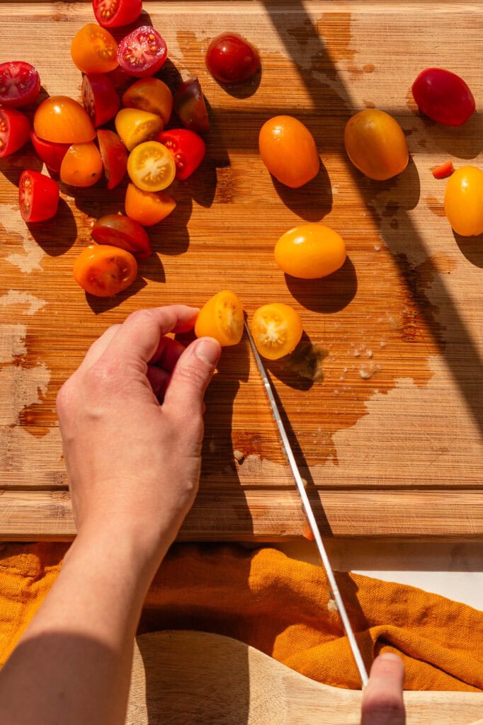 Hands slicing tri-colored cherry tomatoes in half on a wooden cutting board