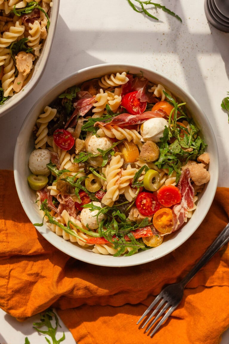 A bowl of Italian Deli Pasta Salad ready to eat sits on a white countertop.