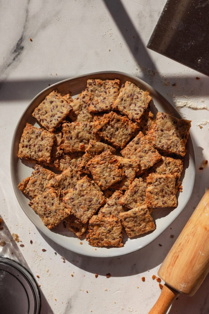 A plate of freshly baked seedy sourdough crackers on a white countertop.