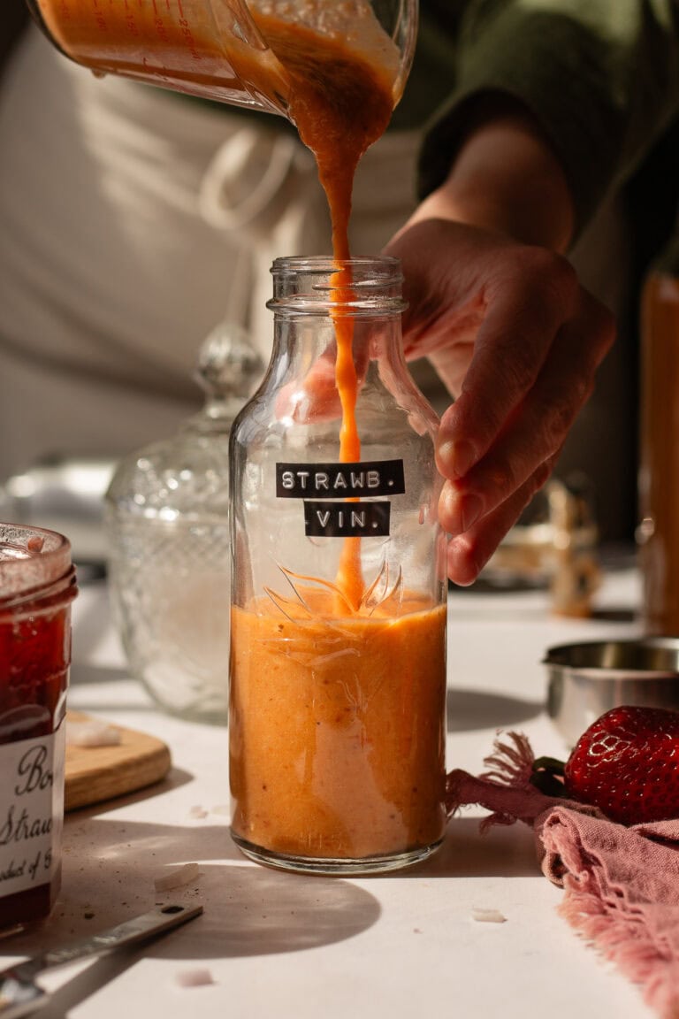 someone pouring the blended salad dressing into an 8-ounce glass bottled labeled "strawberry vin."