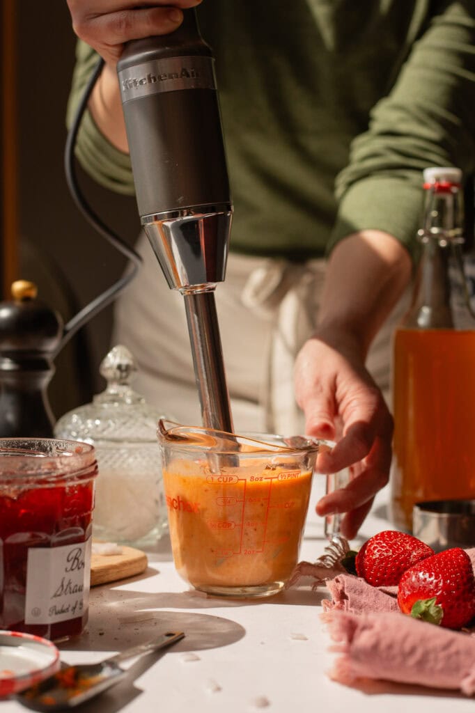 Someone using an immersion (stick blender) to blend all the pepper jelly vinaigrette ingredients into a smooth salad dressing