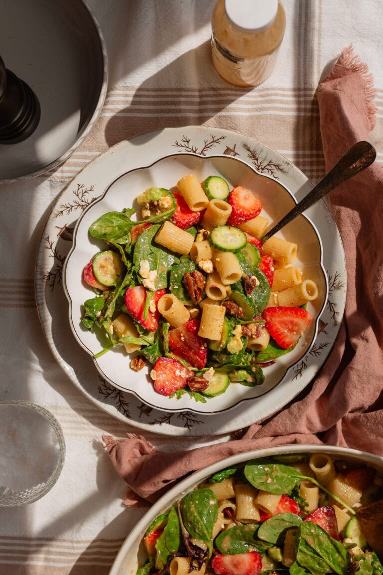 a single serving of cucumber strawberry pasta salad plated on a white ceramic plate with scalloped edges.