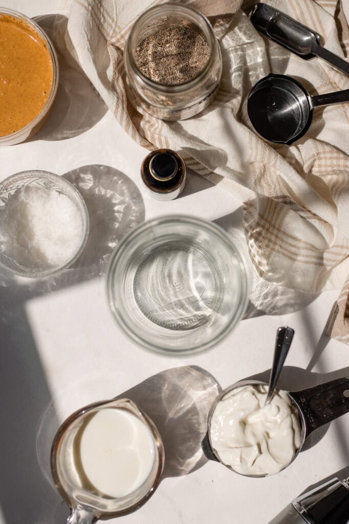 all the ingredients for peanut butter yogurt chia pudding laid out on a counter. There's portioned and measured peanut butter, yogurt, water, vanilla extract, maple syrup and chia seeds.