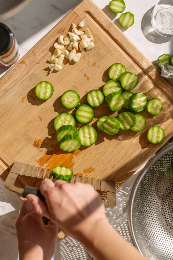 someone using a ripple cutter and wooden cutting board to chop small diameter green pickling cucumbers, the main ingredient in Bloody Mary Pickles.