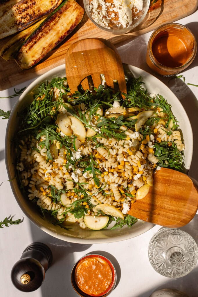 A bowl of our corn and summer squash pasta salad sits on a white counter before dressing is mixed in.
