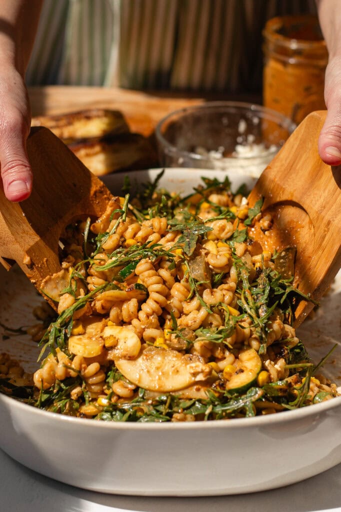 Hands using salad tongs to mix in the salad dressing.