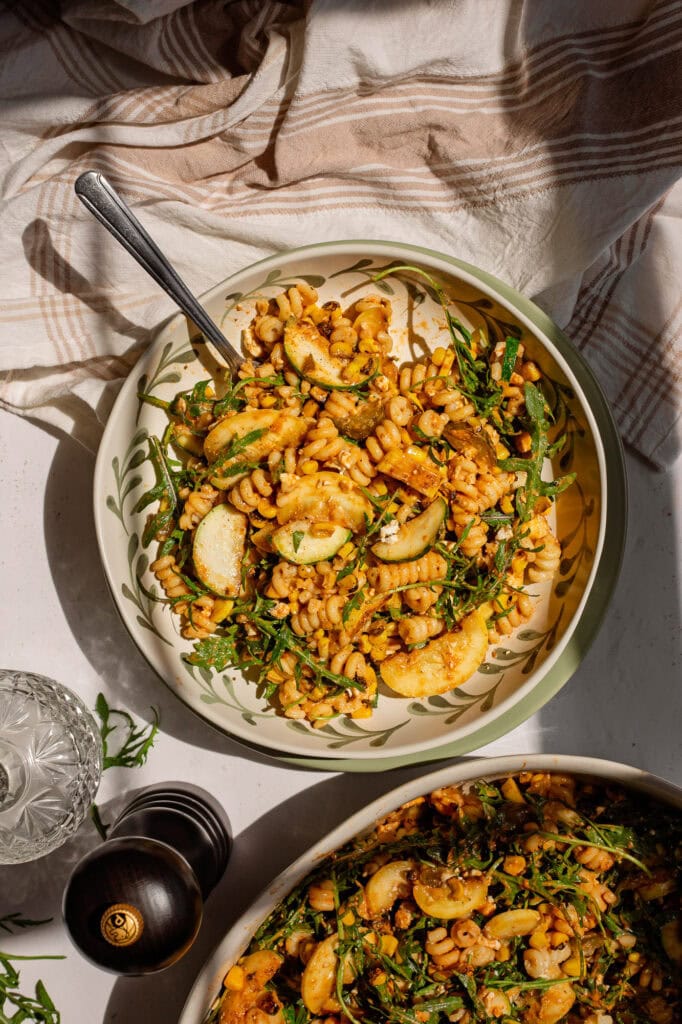 A single serving bowl of our corn and summer squash pasta salad sits on a white counter top.