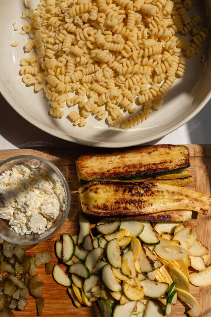 All of the ingredients for this pasta salad including bronze cut pasta, squash and zucchini are laid out on a counter top.