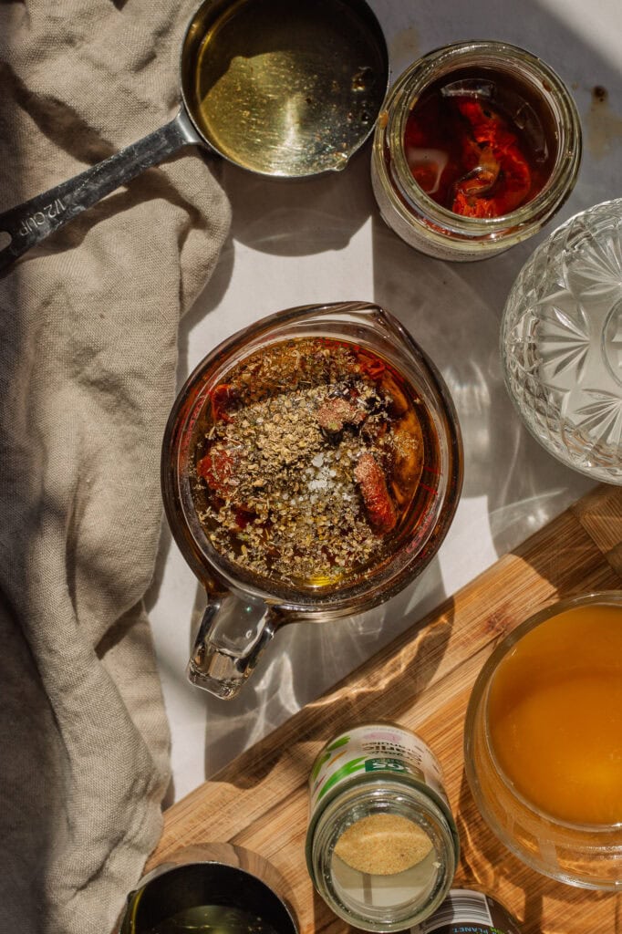All ingredients, including sun-dried tomatoes, fresh cracked pepper and sea salt are shown in a measuring cup on a white counter.