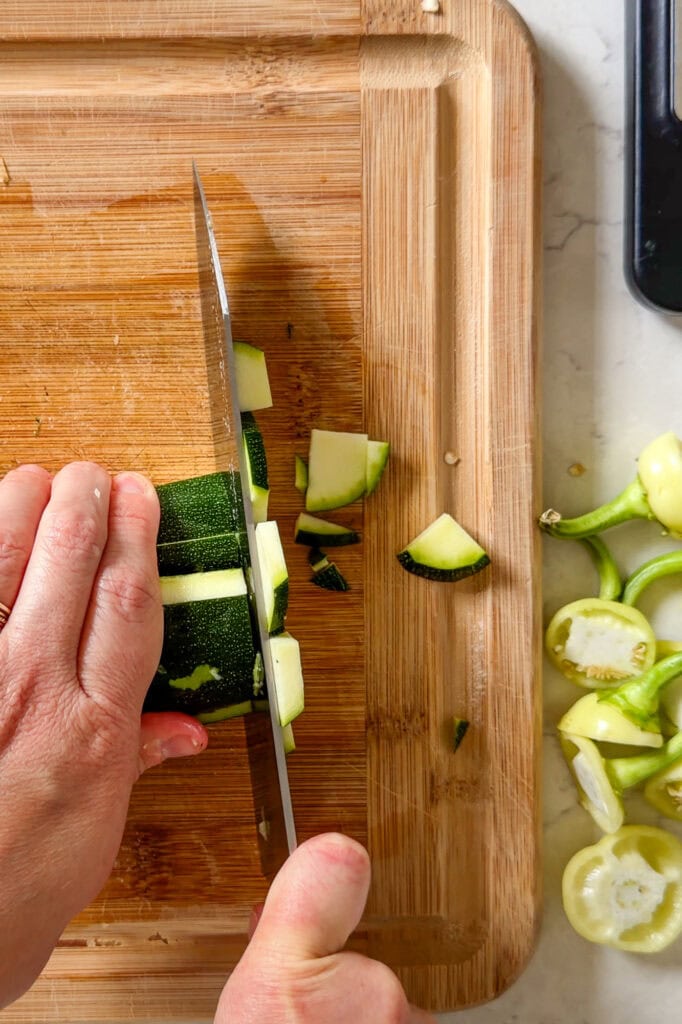 raw zucchini being cut on a wooden cutting board