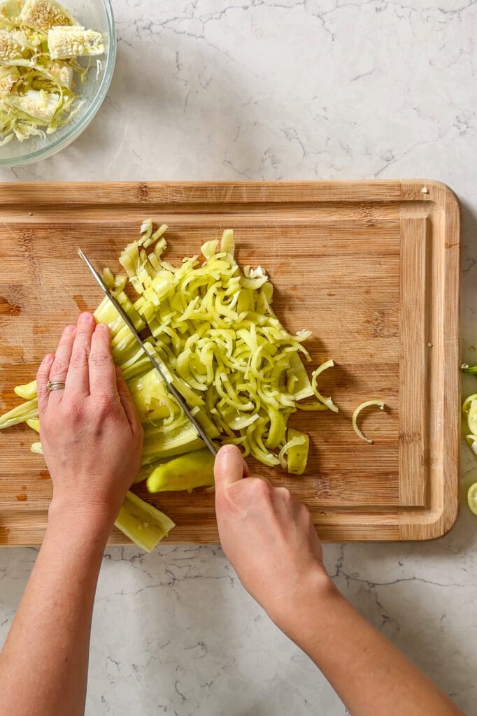 raw banana peppers being cut on a wooden cutting board