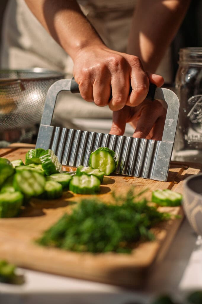 someone using a stainless steel ripple cutter to cut cucumbers into ripple cut pickle chips for fermentation.