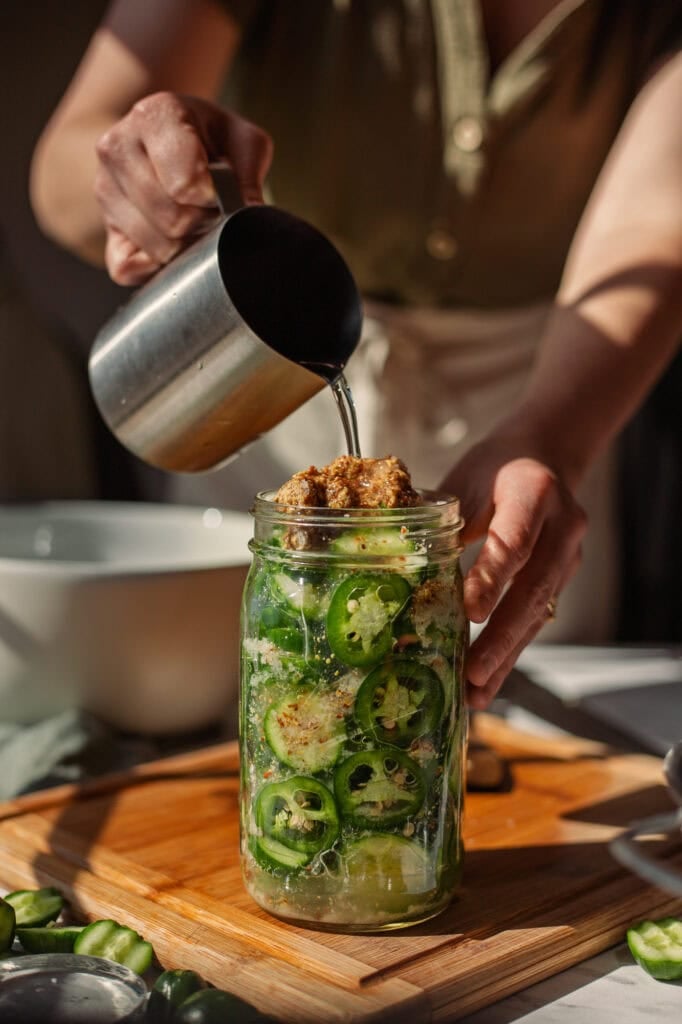 An aluminum cup pours water over the vegetable slices and spoonful of dijon mustard.