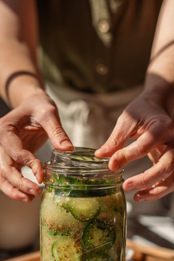 Hands place a glass fermentation weight into a glass jar.
